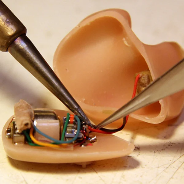 Técnico en electrónica reparando circuito interno de prótesis auditiva con soldador y pinzas de precisión